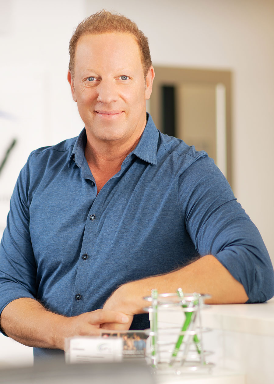 Markus Erl, Geschäftsführer, lächelnd in einem Büro stehend, trägt ein blaues Hemd. Im Hintergrund ist das Logo der Firma MPV erkennbar.