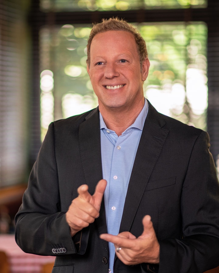 Markus Erl, Geschäftsführer der MPV GmbH, lächelt in einem professionellen Umfeld, gekleidet in einem dunklen Anzug mit hellblauem Hemd. Im Hintergrund sind Fenster und eine entspannte Atmosphäre zu sehen.