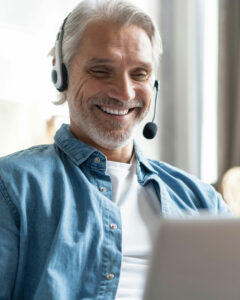 Ein älterer Mann mit grauem Haar, lächelnd, während er ein Headset trägt und auf einem Gerät arbeitet.